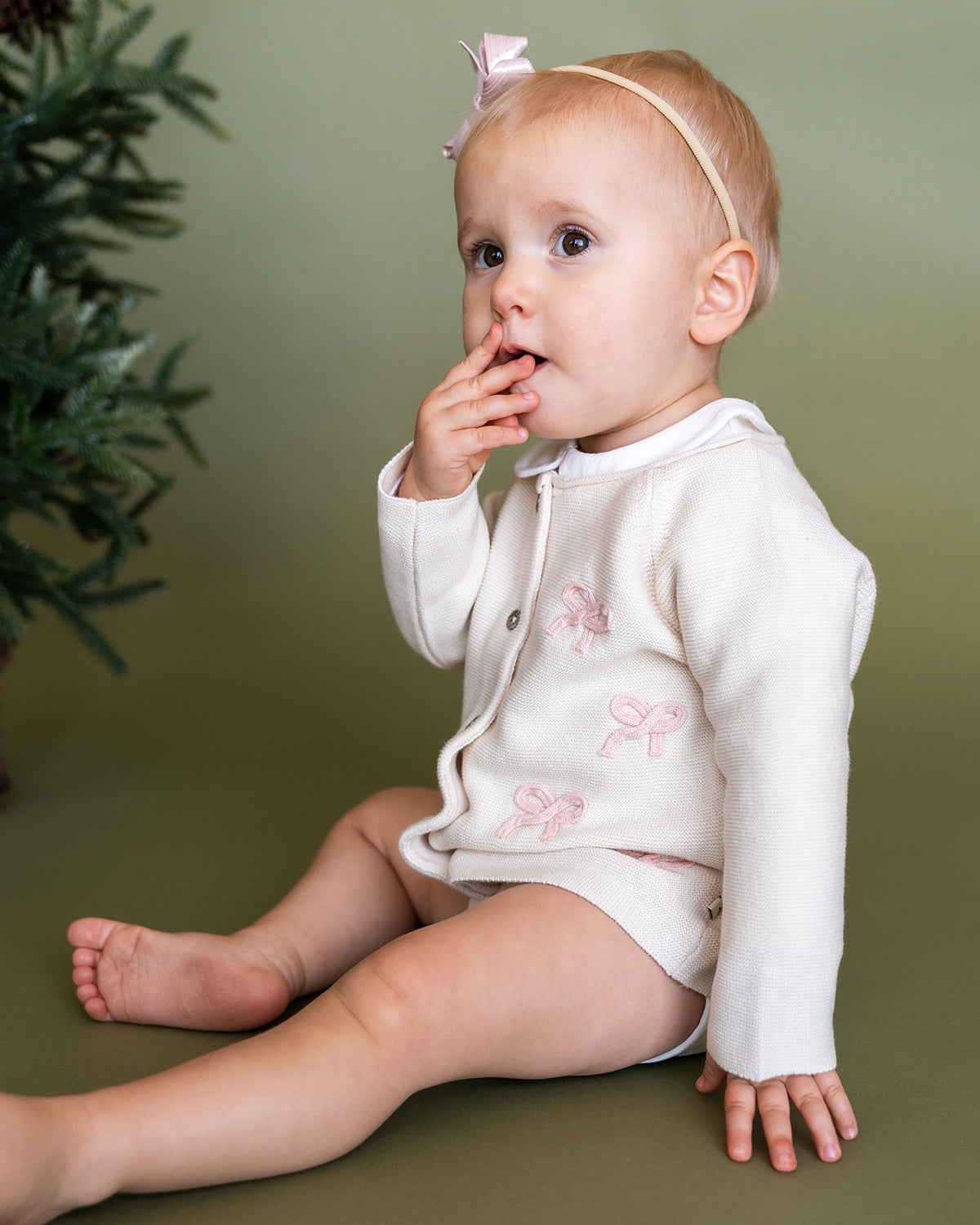 Viverano Organics baby cardigan in white with pink bow embroidery worn by sitting infant girl with headband